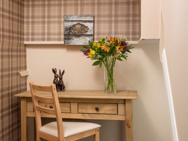 A wooden desk with a chair a vase of flowers and two rabbit sculptures on the desk at Esk View Cottage in Grosmont