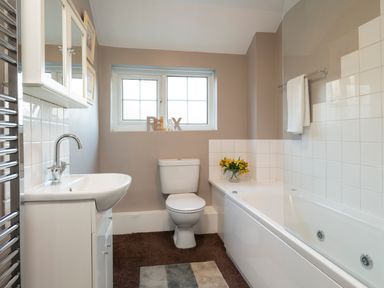 A bathroom with a sink cabinet toilet bathtub with a towel on the rail and flowers on the ledge at Esk View Cottage in Grosmont