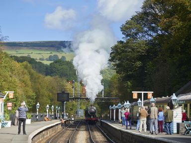 A steam train approaching a platform with passengers waiting and taking photos at Esk View Cottage in Grosmont