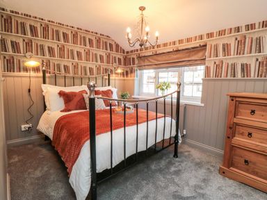 A bedroom with a metal bed frame and orange bedding a wooden dresser and book wallpaper at Esk View Cottage in Grosmont