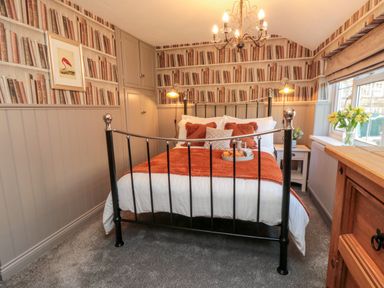A bedroom with a black metal bed frame orange bedding bedside tables and book-patterned wallpaper at Esk View Cottage in Grosmont