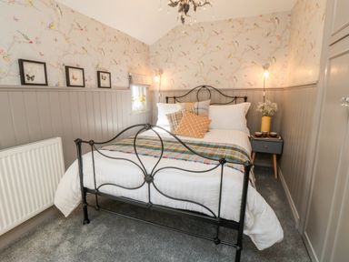 A bedroom with a metal bed frame, patterned pillows, a bedside table, and floral wallpaper at Esk View Cottage in Grosmont