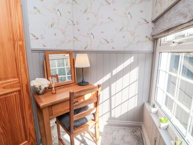 A small wooden desk with a mirror and lamp next to a window with potted plants in a room with bird patterned wallpaper at Esk View Cottage in Grosmont