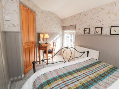 A bedroom with a bed covered with a blanket and a wooden door next to a small wooden desk and chair at Esk View Cottage in Grosmont