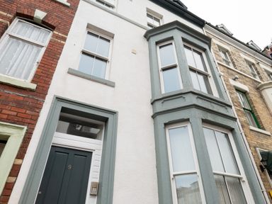 The exterior of a white house with grey trim and a bay window above the door number 19 at Church View Whitby
