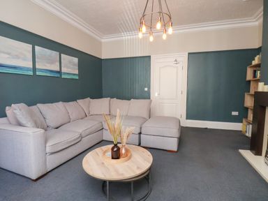 A living room with a grey sectional sofa a round wooden coffee table and blue walls at Church View in Whitby