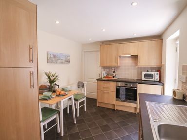 A kitchen with wooden cabinets a small dining table set with plates and croissants and a sink at Church View Whitby