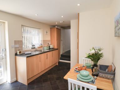 A kitchen with wooden cabinets a sink and a dining table set with plates cups and flowers at Church View in Whitby