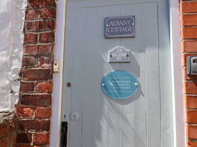 A grey wooden door with three signs including Albany Cottage and Yorkshire Coastal Cottages at Albany Cottage in Whitby