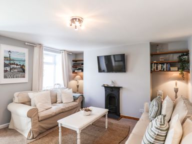 A living room with two sofas a wall-mounted TV and bookshelves at Albany Cottage in Whitby