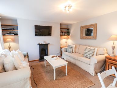 A living room with two beige sofas a white coffee table a wall-mounted TV a small black fireplace wooden shelves and lamps at Albany Cottage in Whitby
