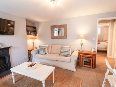 A living room with a beige sofa two side tables with lamps a white coffee table and a wall-mounted tv at Albany Cottage in Whitby