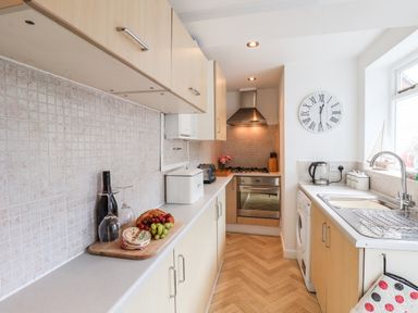 A kitchen with wooden cabinets a stove a sink a washing machine and a countertop with bread cheese grapes and wine at Albany Cottage in Whitby