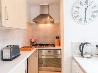 A kitchen corner with a gas stove oven extractor toaster kettle wooden utensil holder and a wall clock at Albany Cottage in Whitby