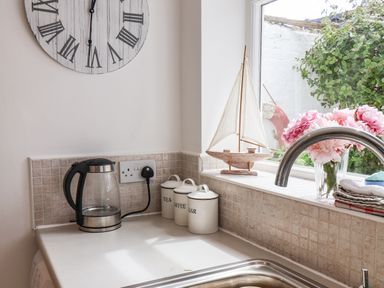 A kitchen countertop with an electric kettle canisters labeled tea coffee and sugar a sailboat model flowers in a vase and a kitchen sink with a faucet at Albany Cottage in Whitby