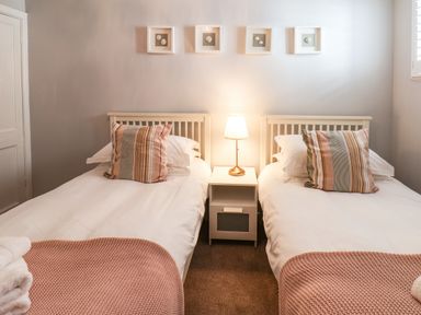 A bedroom with two single beds a nightstand with a lamp and framed pictures on the wall at Albany Cottage in Whitby