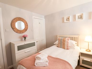 A bedroom with a single bed a bedside table with lamp a chest of drawers with flowers and a round mirror on the wall at Albany Cottage in Whitby