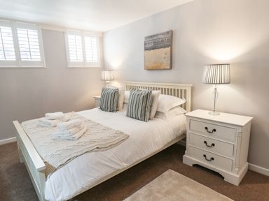 A bedroom with a white bed with striped pillows two bedside tables with lamps and folded towels at Albany Cottage in Whitby