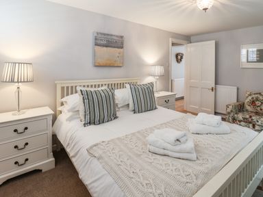 A bedroom with a double bed and striped pillows two bedside tables with lamps a floral armchair and folded towels on the bed at Albany Cottage in Whitby