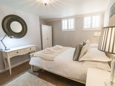 A bedroom with a double bed with pillows and towels a white desk with a lamp a round mirror a wardrobe and two windows at Albany Cottage in Whitby