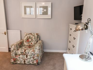 A floral armchair next to a white dresser with a lamp and a mounted TV on the wall at Albany Cottage in Whitby