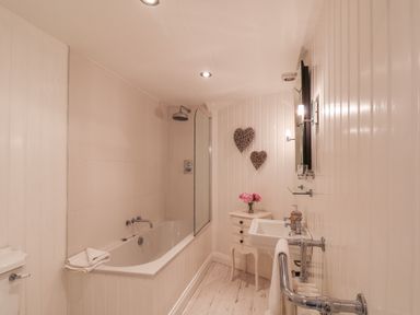 A bathroom with a bathtub shower sink small table with flowers and heart decorations on the wall at Albany Cottage in Whitby