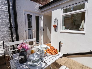 An outdoor patio with a white table and chairs set with croissants plates bowls cups and flowers at Albany Cottage in Whitby