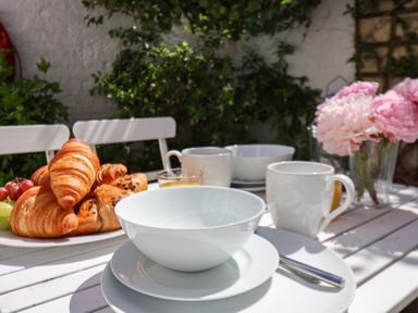 A white table set outdoors with croissants fruit white bowls cups and pink flowers Albany Cottage in Whitby