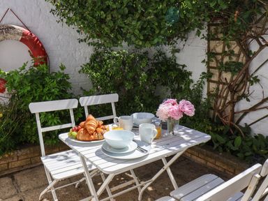 An outdoor patio with a white table and chairs set with croissants fruit cups and flowers at Albany Cottage in Whitby