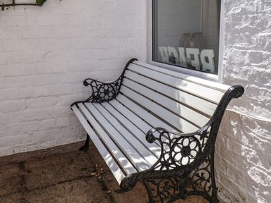 A white bench with black ornate metal armrests against a white brick wall near a window at Albany Cottage in Whitby