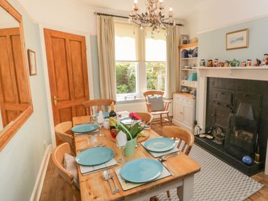 A dining room with a wooden table set for six near a window and a fireplace at Arden House in Whitby