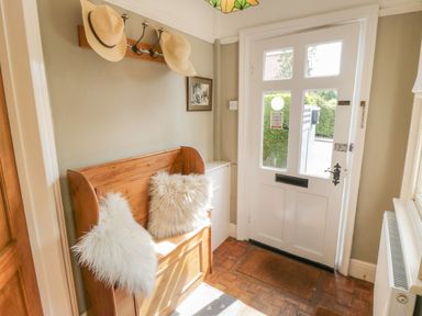 An entrance hall with a white door wooden bench with cushions hats hanging on hooks and a radiator at Arden House Whitby