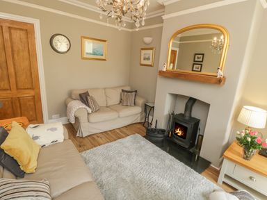 A living room with two sofas a wood burning stove a mirror above the fireplace and a wooden side table with a vase of flowers at Arden House Whitby