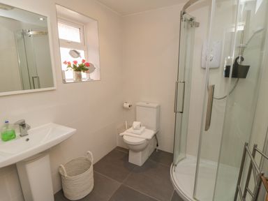 A bathroom with a sink a toilet a shower enclosure a window with flowers and a mirror at Arden House in Whitby