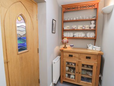 A wooden cabinet with dishes and cups and a small stained glass lamp beside a wooden door with a stained glass panel at Arden House in Whitby