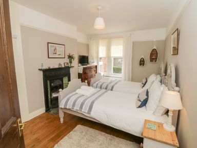 A bedroom with two single beds a wooden dresser a fireplace and a window at Arden House in Whitby