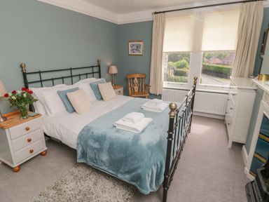 A bedroom with a double bed with folded towels bedside tables a wooden chair a chest of drawers and a window with blinds at Arden House Whitby