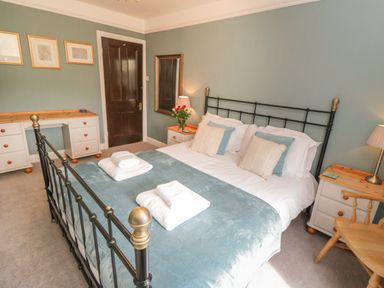 A bedroom with a black metal bed, bedside tables, desk, mirror, and wooden chair at Arden House in Whitby
