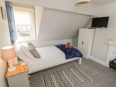 A bedroom with a single bed, bedside table with lamp, wardrobe, wall-mounted TV, and a rug on the floor at Arden House in Whitby