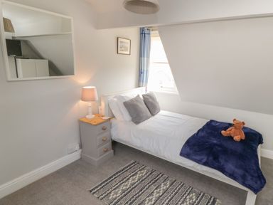 A bedroom with a single bed and bedside table with lamp and a mirror on the wall at Arden House in Whitby
