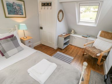 A bedroom with a bed pillows and blanket nightstand with lamp wooden floor and armchair near a window at Arden House in Whitby