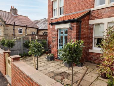 An outdoor front patio area with a tiled floor small trees in pots a blue door and brick walls at Arden House Whitby