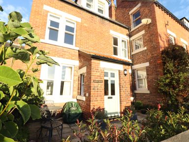 The front of a brick house with a white door and windows a small patio area with two chairs and a table and plants at Arden House Whitby