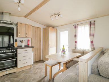 A kitchen and dining area with a stove cabinets dining table bench seating and a window with curtains at The Hideaway in Cockermouth