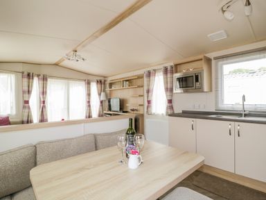 An open kitchen and dining area with a wooden table wine bottle glasses and a small flower vase at The Hideaway in Cockermouth