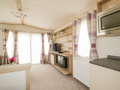 A living room with a television fireplace shelves and plaid curtains at The Hideaway in Cockermouth