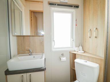 A bathroom with a sink, mirror, toilet, window, and wooden cabinets at The Hideaway in Cockermouth
