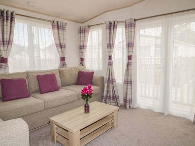 A living room with a beige sofa and purple cushions and a wooden coffee table with a vase of pink flowers at The Hideaway in Cockermouth