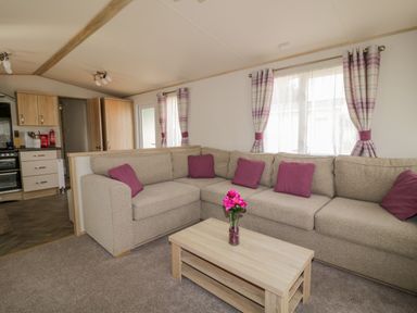 A living room with a beige corner sofa with purple cushions and a wooden coffee table with a vase of flowers at The Hideaway in Cockermouth