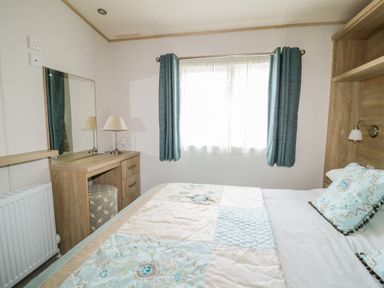 A bedroom with a bed a desk and a window with curtains at The Hideaway in Cockermouth